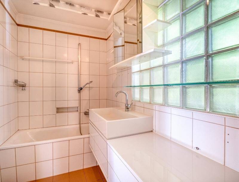 Badezimmer mit Badewanne, modernem Waschbecken und einer Glasbausteinwand für natürliches Licht.
