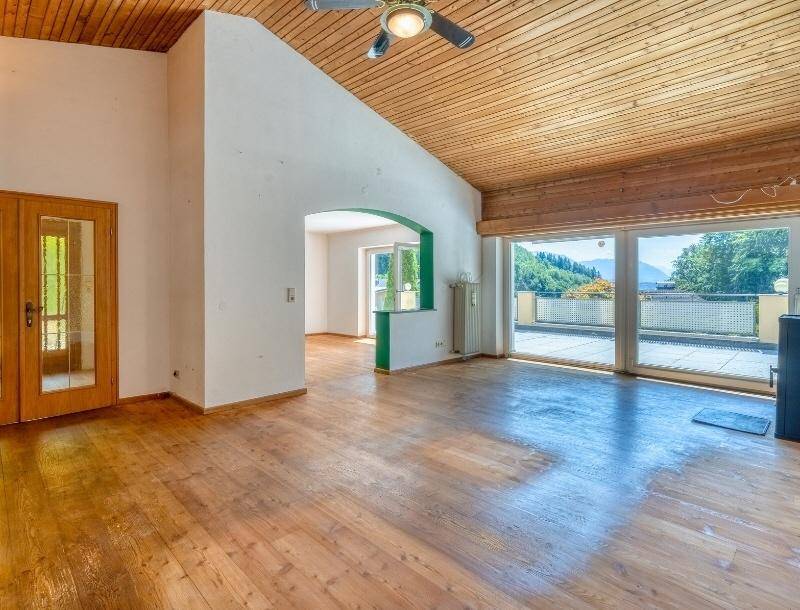 Helles Wohnzimmer mit Holzboden, Holzdecke und großen Fenstern mit Zugang zur Terrasse und Bergblick.