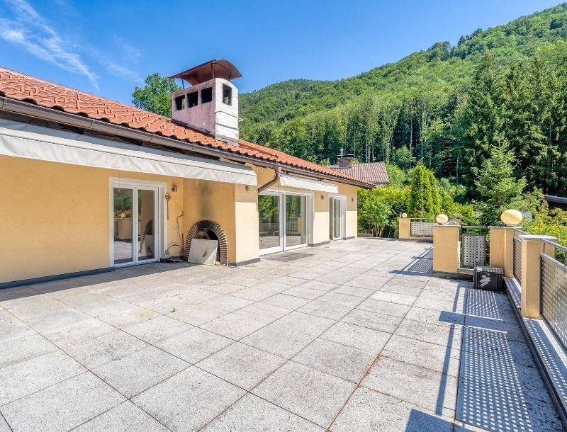 Große, geflieste Terrasse entlang der Hausfassade mit mehreren Zugängen und einem Außenkamin.
