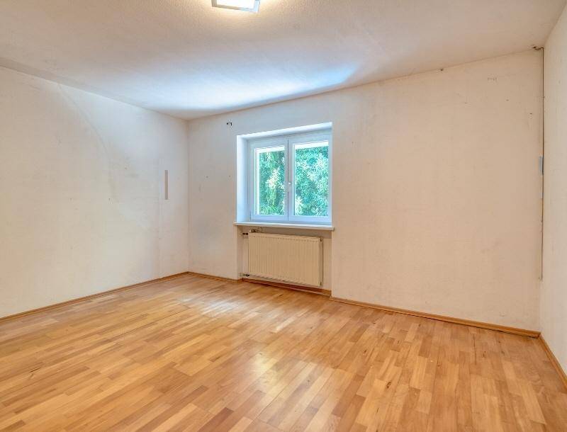 Leeres Zimmer mit Holzboden, weiß gestrichenen Wänden und einem Fenster für Tageslicht.