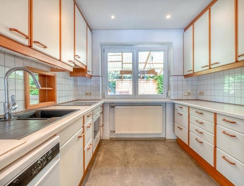 Funktionale Küche mit weißen Schränken, integrierten Geräten und einem Fenster mit Blick ins Grüne.