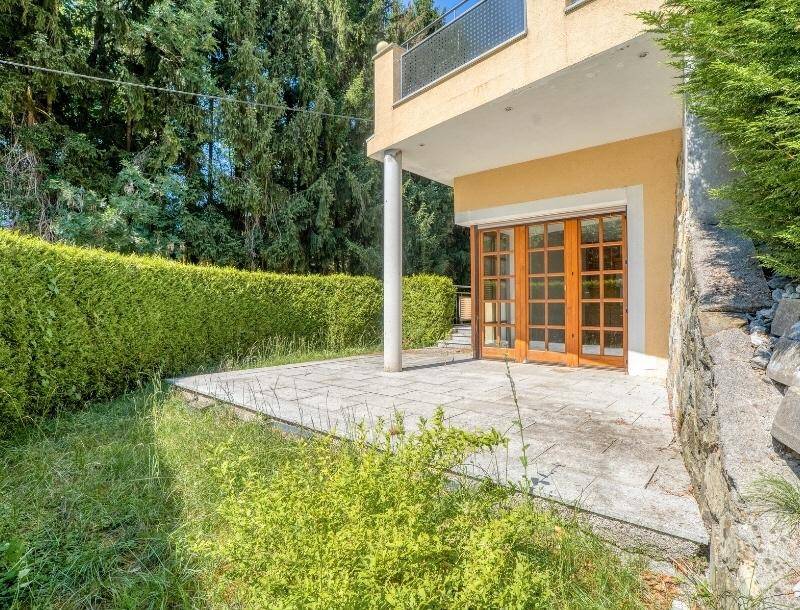 Erdgeschoss-Terrasse mit Steinfliesen und direktem Zugang zum Gartenbereich mit Hecke.