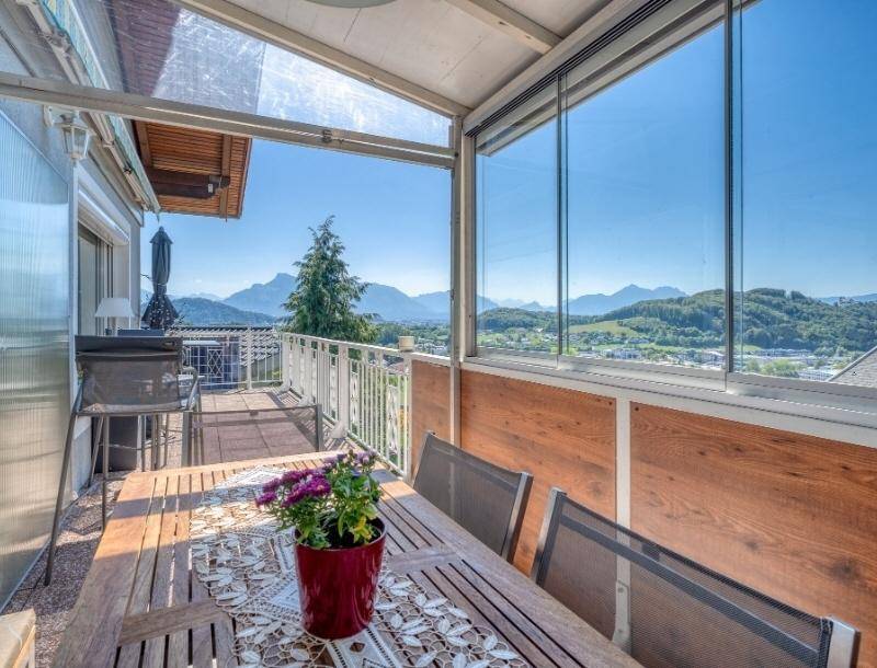 Verglaster Balkon mit Esstisch und Stühlen, bietet einen weiten Blick auf die umliegende Berglandschaft.