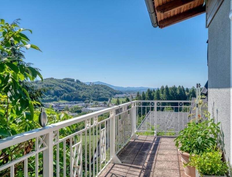 Heller Balkon mit weißem Geländer und Topfpflanzen, bietet einen schönen Blick auf grüne Hügel.
