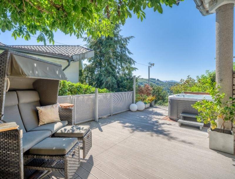 Sonnige Terrasse mit bequemen Outdoor-Möbeln und einem Whirlpool, umgeben von grünen Pflanzen.