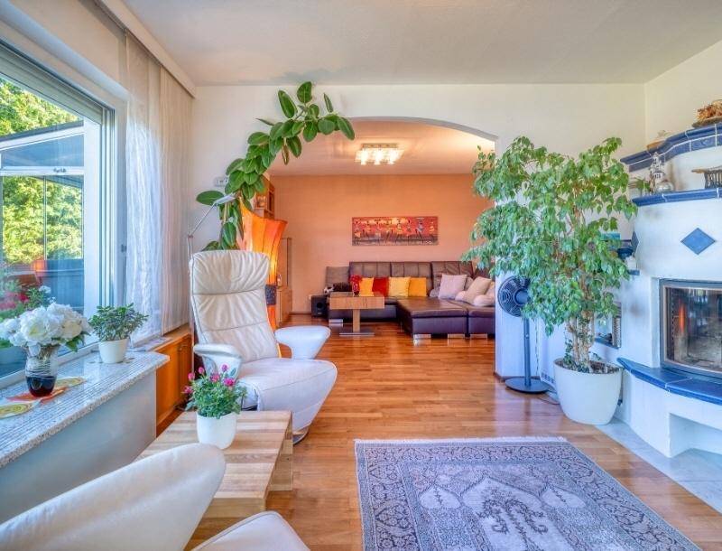 Gemütliches Wohnzimmer mit Holzboden, Kamin und großen Fenstern, die viel Tageslicht hereinlassen.