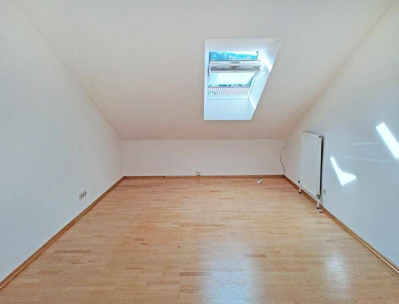 Lichtdurchfluteter Dachgeschossraum mit Holzboden, Dachschrägen und einem großen Dachfenster.
