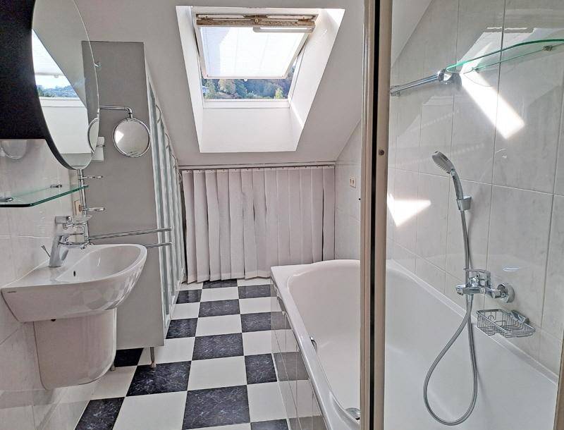 Modernes Badezimmer mit schwarz-weißem Fliesenboden, Badewanne, Dusche und Dachfenster.