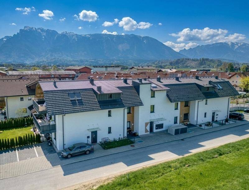 Moderne Reihenhäuser mit dunklen Dächern und weißer Fassade vor beeindruckender Bergkulisse.