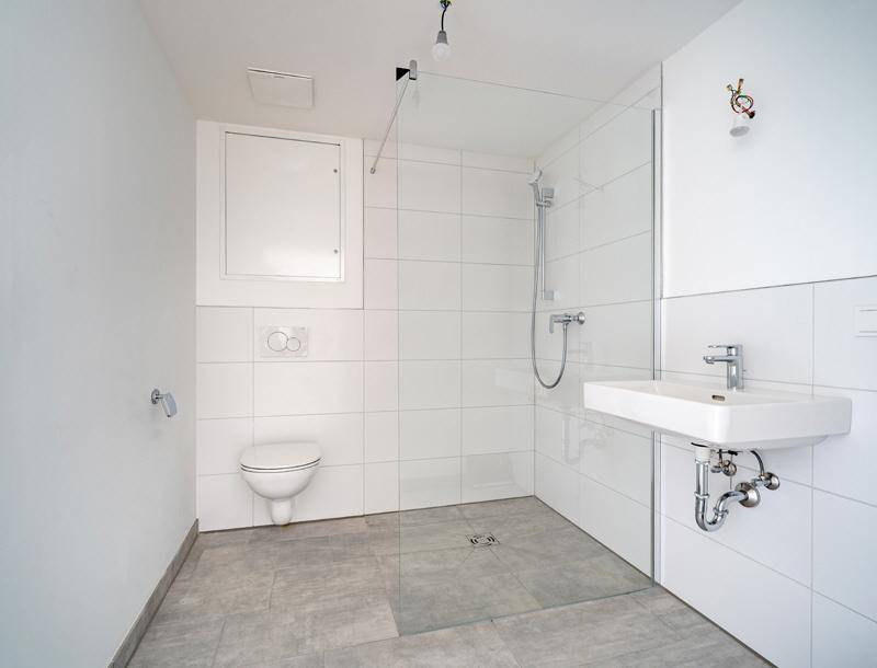 Modernes Badezimmer mit weißen Fliesen, bodengleicher Dusche und wandhängendem WC.