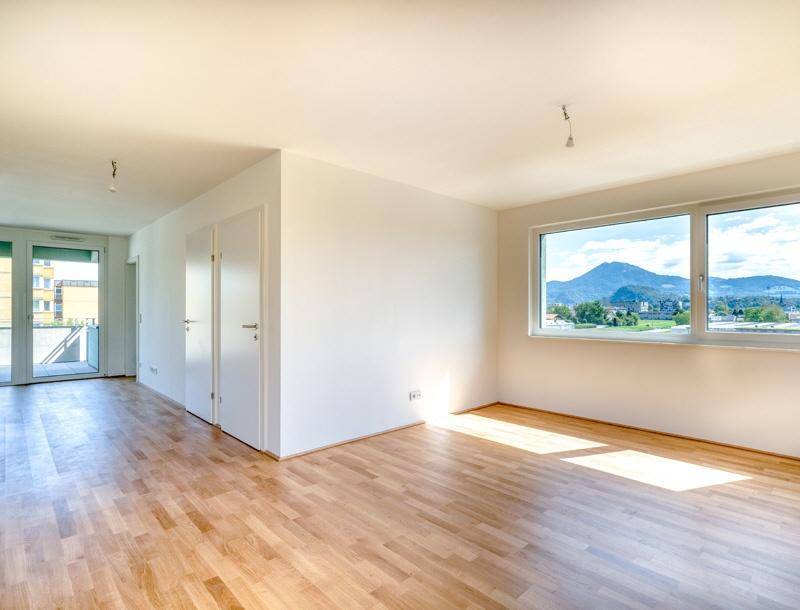 Heller Wohnraum mit Holzboden, großen Fenstern und Zugang zu einem Balkon mit Bergblick.
