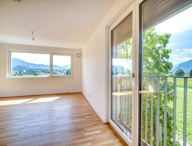 Lichtdurchfluteter Wohnbereich mit Holzboden und direktem Zugang zu einem Balkon mit Grünblick.