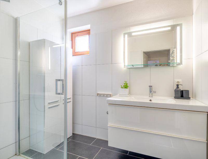 Modernes Badezimmer mit ebenerdiger Dusche, elegantem Waschtisch und beleuchtetem Spiegel.