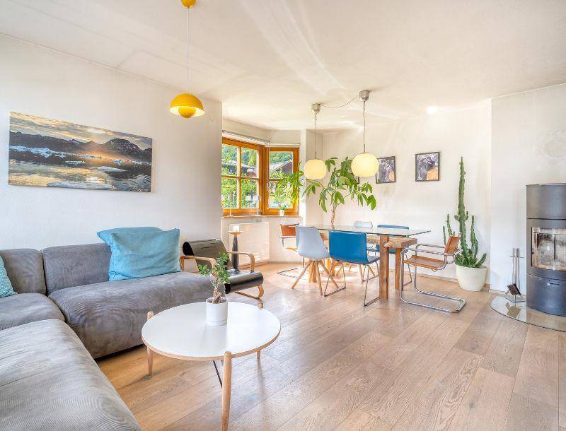 Heller Wohn-Essbereich mit Holzboden, gemütlichem Sofa, modernem Kaminofen und Blick ins Grüne.