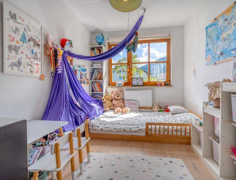 Gemütliches Kinderzimmer mit Holzbett, Spielbereich und einem schönen Blick auf die Berge.