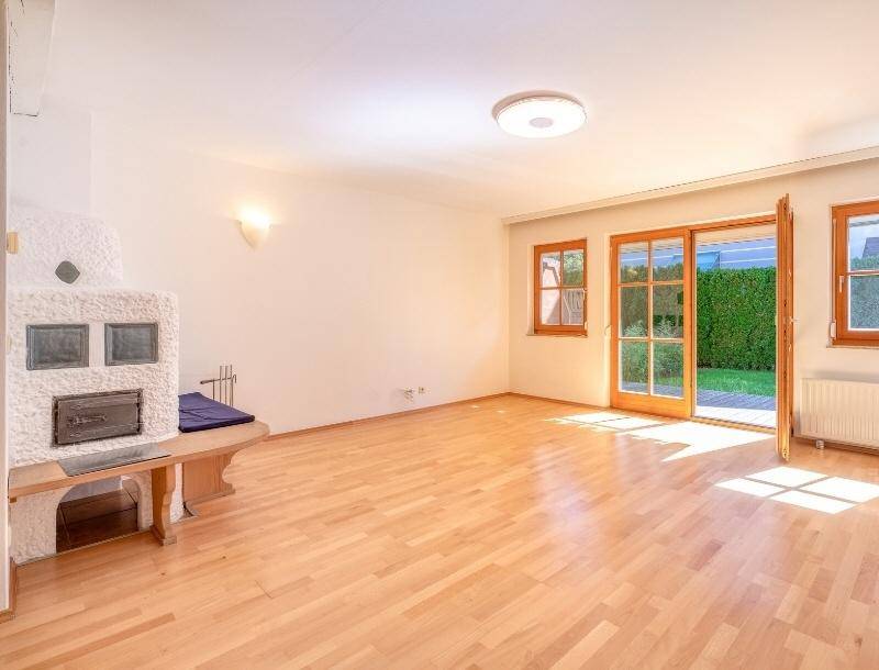 Helles Wohnzimmer mit traditionellem Kachelofen, Holzboden und Zugang zum Garten.