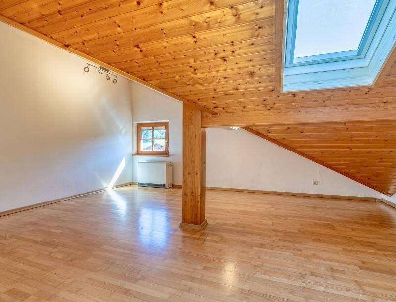 Geräumiges Dachzimmer mit Holzbalken, Holzdecke, Holzboden und einem großen Dachfenster.