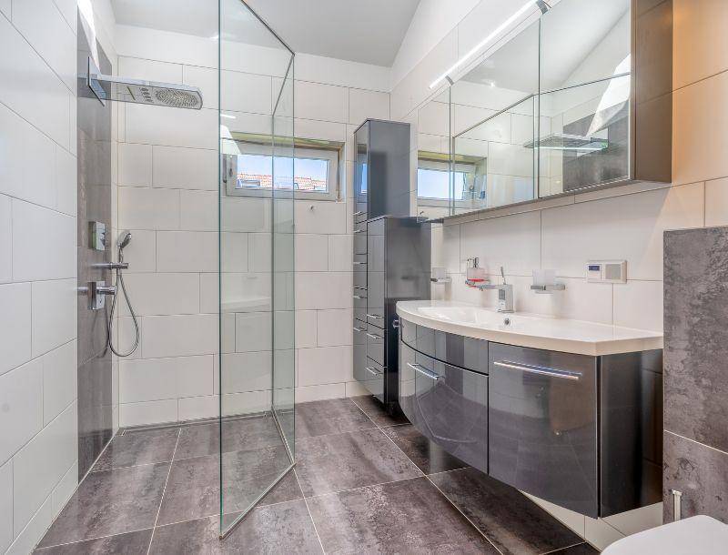 Modernes Badezimmer mit begehbarer Glasdusche, Waschtischunterschrank und Fenster für Tageslicht.