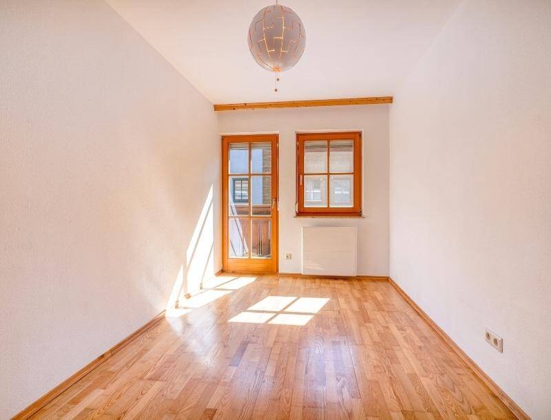 Helles Zimmer mit Holzboden und Zugang zu einem Balkon, gut beleuchtet.