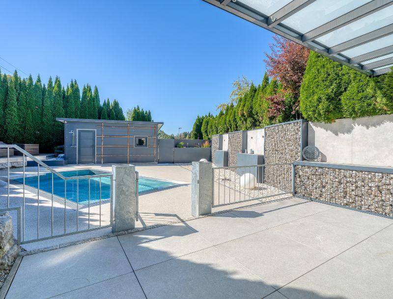 Gepflegter Gartenbereich mit Pool, einem kleinen Nebengebäude und üppiger Heckenbepflanzung.