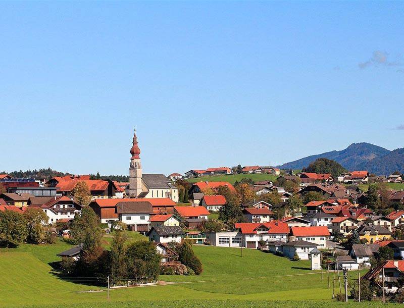 Malerische Ansicht eines Dorfes mit traditioneller Kirche, umgeben von grünen Hügeln und Bergen.