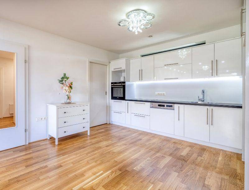 Helle, moderne Küche mit weißen Hochglanzfronten, integrierten Geräten und Holzboden.
