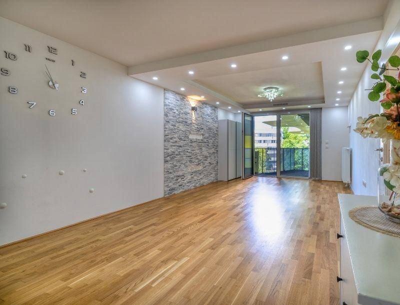 Geräumiges Wohnzimmer mit Holzboden, moderner Wandgestaltung und Zugang zu einem Balkon.