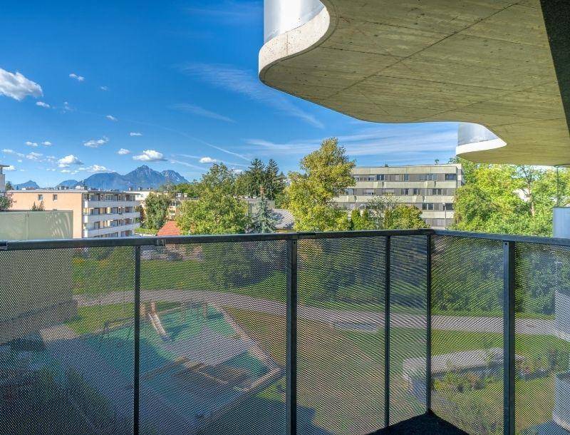Balkon mit Blick auf einen Spielplatz, grüne Umgebung und die majestätischen Berge im Hintergrund.