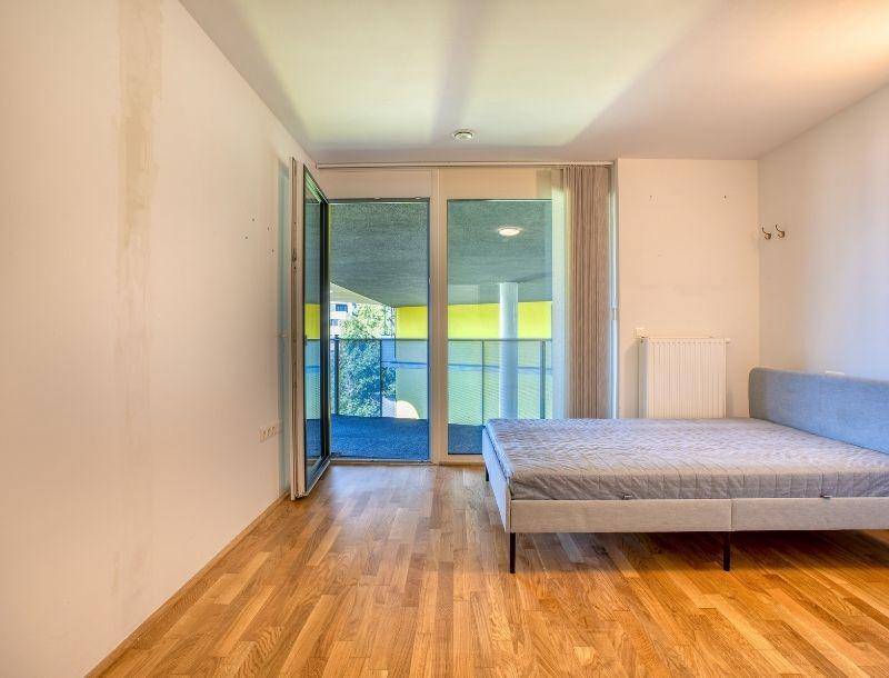 Schlafzimmer mit Holzboden, Bett und direktem Zugang zu einem sonnigen Balkon.