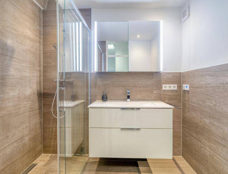 Modernes Badezimmer mit begehbarer Dusche, eleganten Fliesen und beleuchtetem Spiegelschrank.
