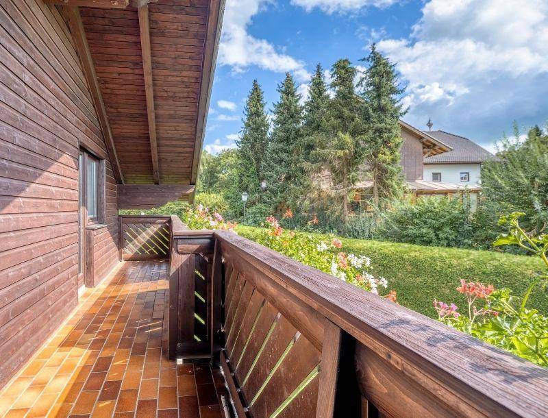 Geräumiger Holzbalkon mit Ziegelboden und Blick ins Grüne, umgeben von Blumen.