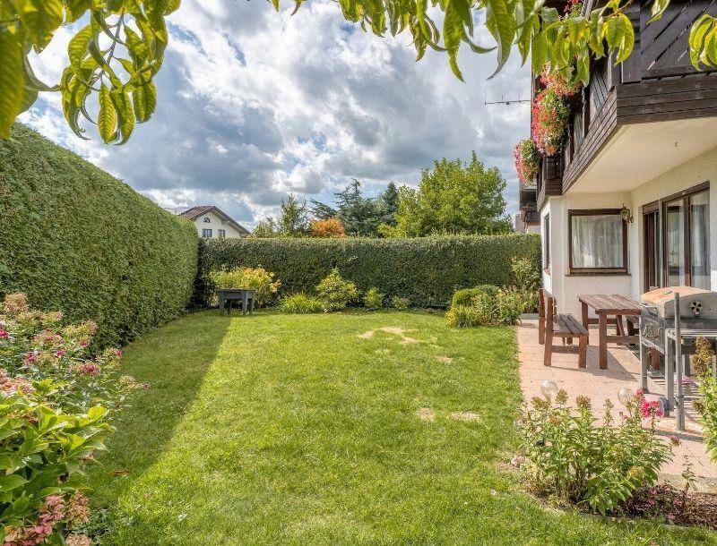 Weitläufiger Garten mit Rasenfläche und angrenzender Terrasse, umgeben von hohen Hecken.