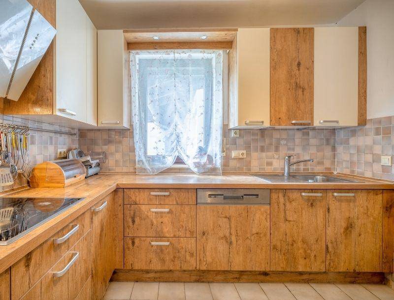 Funktionale Küche mit Holzfronten, hellen Oberschränken und Fliesenboden.