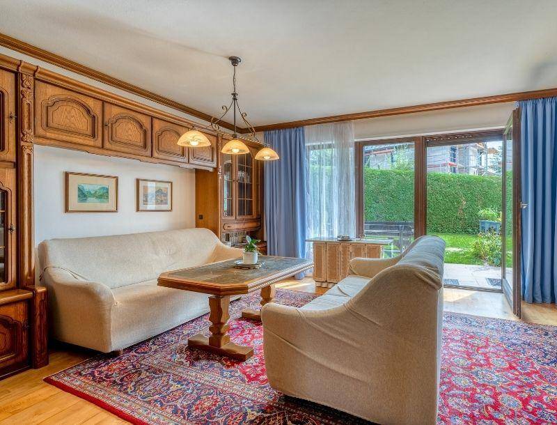 Traditionelles Wohnzimmer mit Holzvertäfelung, beigem Sofa und Zugang zum Garten.