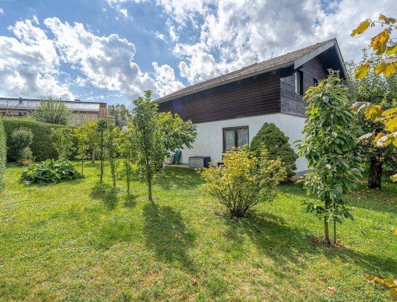 Rückseite des Hauses mit Garten, umgeben von Bäumen und Sträuchern unter bewölktem Himmel.