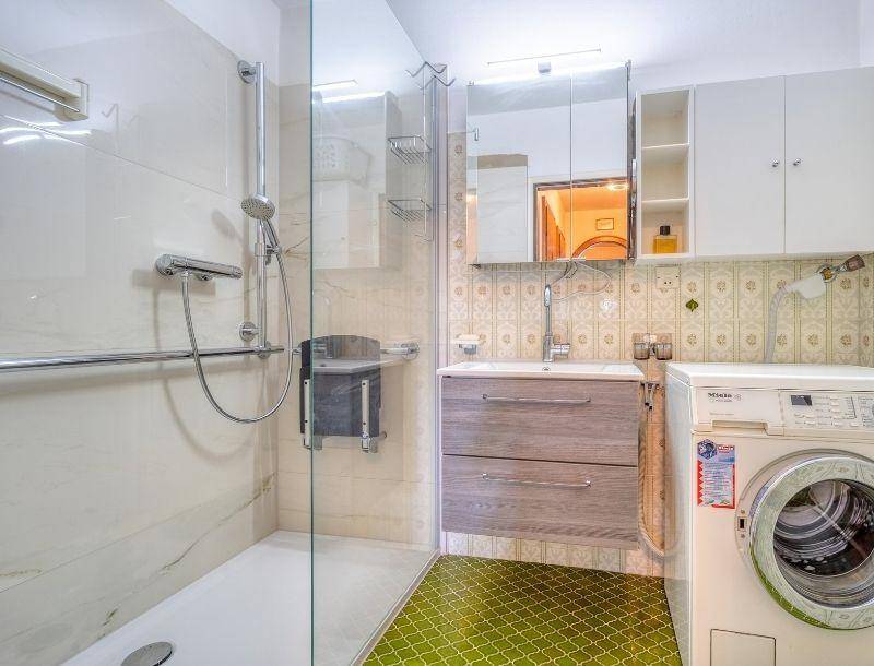 Modernes Badezimmer mit ebenerdiger Dusche, Haltegriffen und Waschmaschine.