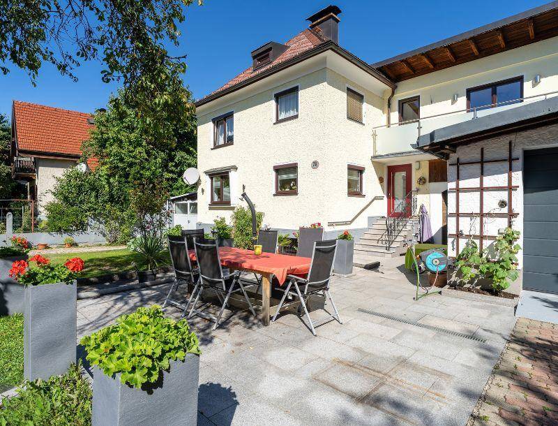 Charmantes Haus mit großer gepflasterter Terrasse und grünem Garten, ideal für entspannte Stunden im Freien.