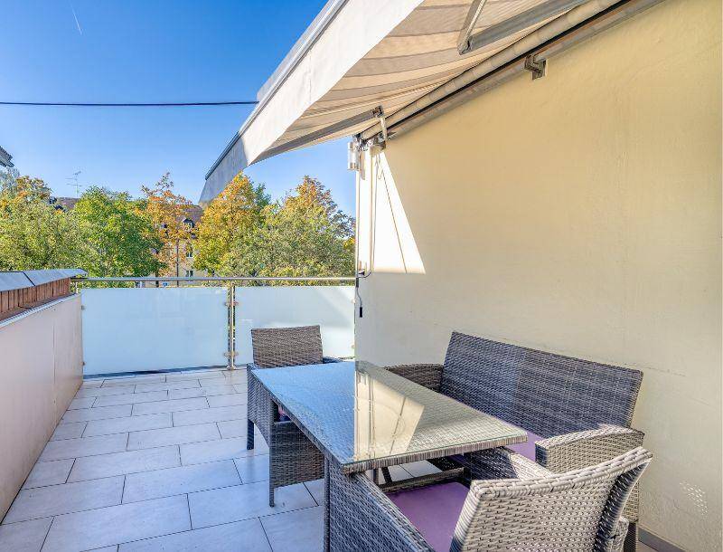 Gemütlicher Balkon mit Rattanmöbeln und ausfahrbarer Markise, ideal für entspannte Stunden im Freien.