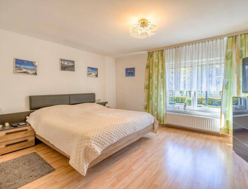Helles Schlafzimmer mit großem Doppelbett, Laminatboden und Fenster mit grünen Vorhängen für viel Tageslicht.