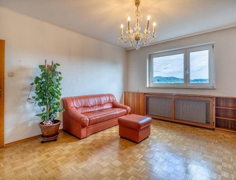 Helles Wohnzimmer mit orangefarbenem Sofa, Parkettboden und einem Fenster mit Ausblick.