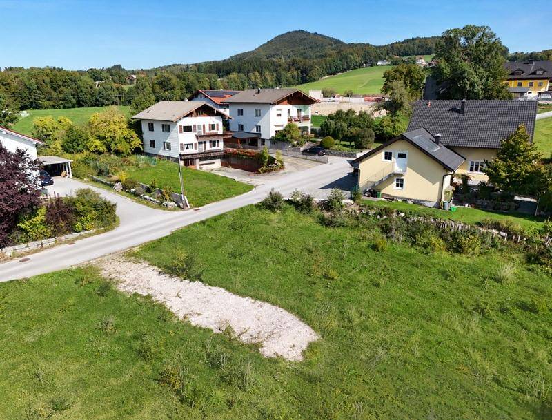 Luftaufnahme eines Baugrundstücks in ländlicher Umgebung mit bestehenden Häusern im Hintergrund.