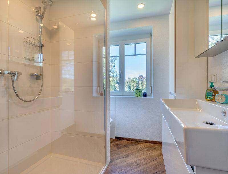 Modernes Badezimmer mit begehbarer Dusche, weißem Waschbecken und Fenster.