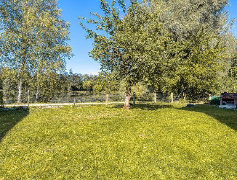 Gepflegter Garten mit Rasenfläche, Bäumen und Blick auf einen nahegelegenen See.