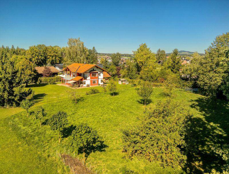 Idyllische Grünfläche mit Obstbäumen und einem traditionellen Haus im Hintergrund, umgeben von Natur.