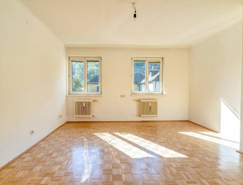 Heller Raum mit Parkettboden und zwei Fenstern, die viel natürliches Licht hereinlassen.