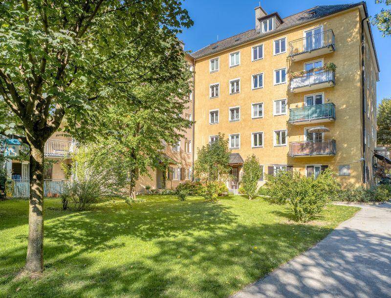 Gelbes Mehrfamilienhaus mit Balkonen und einem gepflegten Vorgarten mit Rasen und Bäumen.
