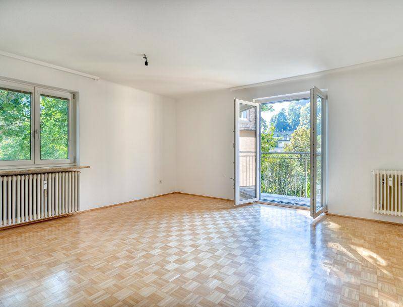 Helles Wohnzimmer mit Parkettboden, weißen Wänden und Zugang zu einem kleinen Balkon.