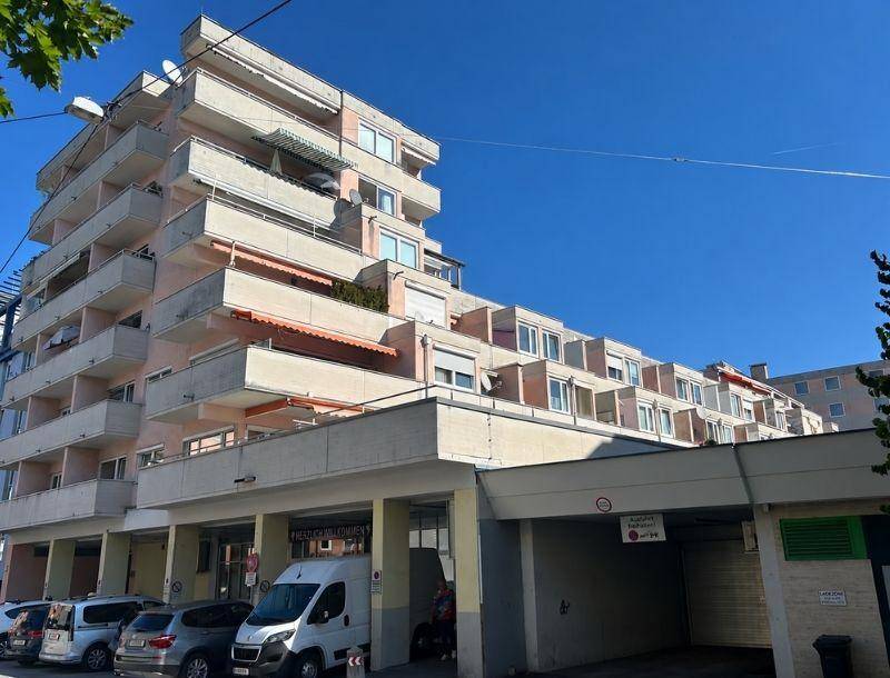 Mehrstöckiges Wohngebäude mit zahlreichen Balkonen und Tiefgaragenzufahrt unter blauem Himmel.