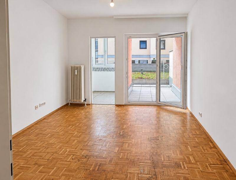 Leeres Wohnzimmer mit Fischgrätparkett, weißen Wänden und Zugang zur Terrasse.