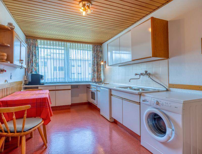 Küche mit Holzdecke, Einbauschränken und Waschmaschine unter dem Fenster.